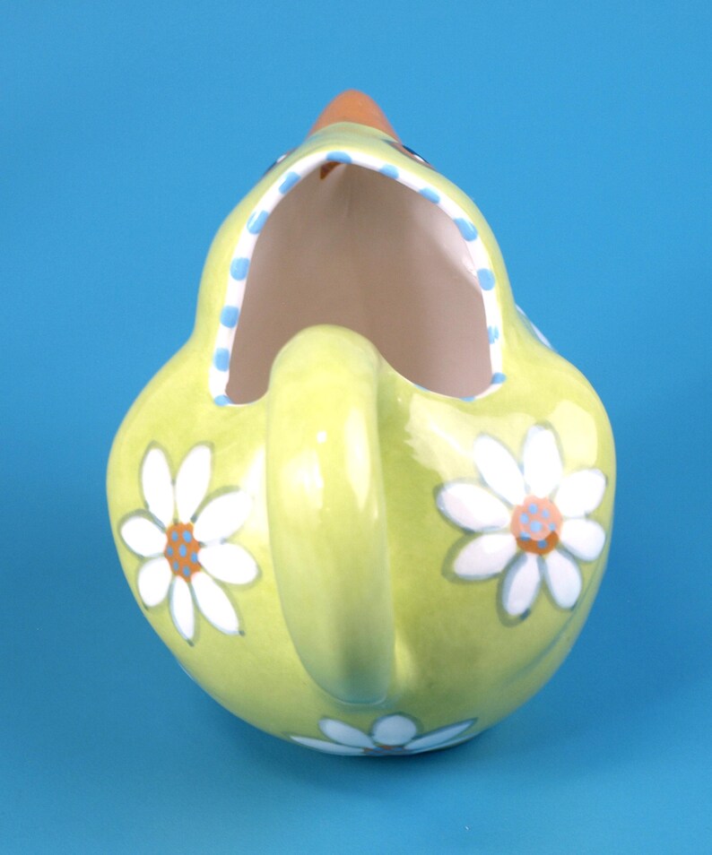 Puede incluir: Jarra de cer&aacute;mica verde claro con asa, con forma de gallina. Decorada con margaritas blancas y un borde de lunares azules. El pico es naranja. Ideal para servir bebidas.