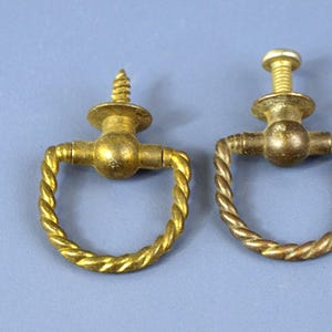 May include: Two antique brass drawer pulls with a twisted rope design. Each pull features a circular handle and a screw for fixing. The brass has a warm, aged patina, indicating they are vintage.