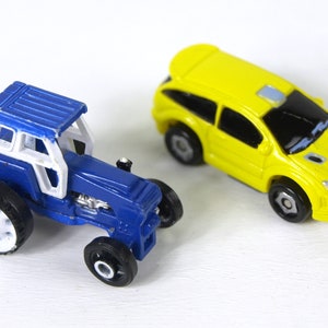 May include: A blue toy tractor with white wheels and a yellow toy car with black wheels.