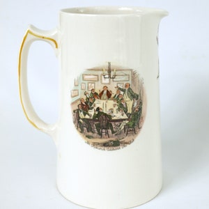 May include: Cream-colored ceramic pitcher with a handle and a spout. The pitcher features a colorful illustration of a group of men around a table, with the text "Mr. Pickwick Addresses The Club". The handle has a gold trim.