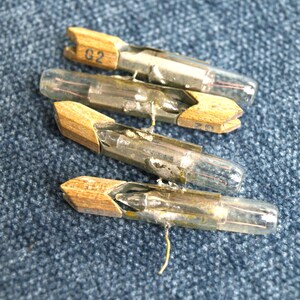 May include: Four vintage glass vacuum tubes with wooden holders. The tubes are clear glass with metal wires inside. One of the tubes has the text "G2" printed on the holder.