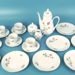 以下が含まれることがあります： 白い磁器のティーセット一式。バラの花柄のデザイン。カップ、ソーサー、プレート、ティーポット、クリーマー、砂糖入れが含まれています。花柄のデザインはピンクのバラと緑の葉が特徴です。