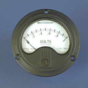 May include: A round Westinghouse analog voltmeter with a black metal frame and a white face. The gauge features a scale from 0 to 1, labeled VOLTS and DIRECT CURRENT, with the text MADE IN USA, STYLE 1161054, and F.S.=1 M.A. printed on it.