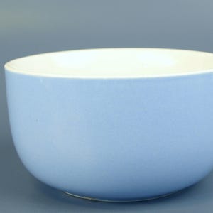 Könnte beinhalten: Eine hellblaue Keramikschale mit weißem Innenraum. Die Schale hat eine abgerundete Form und eine glatte, matte Oberfläche. Die Schale wird wahrscheinlich zum Servieren von Speisen oder als Dekorationsartikel verwendet.