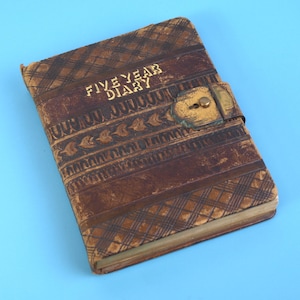May include: A vintage brown leather five-year diary with a decorative embossed pattern and a metal clasp. The cover features the words "FIVE YEAR DIARY" in gold lettering. The diary has a worn, antique appearance.