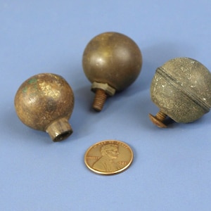 以下が含まれることがあります： 茶色と緑色の様々な色合いの、ねじ付きポストが付いた3つのアンティーク真鍮ボールフィニアル。サイズの比較のためにペニーが含まれています。フィニアルは、家具または装飾品からのものである可能性があります。