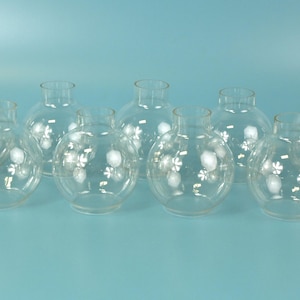 May include: A collection of fourteen clear glass globes, each featuring a small opening at the top and a rounded body. The glass is transparent and smooth, with a uniform spherical shape designed for use as replacement lamp shades or covers.