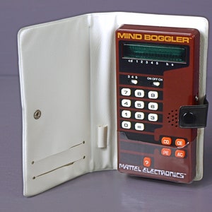 Op de afbeelding: Een bruin handzaam elektronisch spel genaamd "Mind Boggler" van Mattel Electronics. Het spel heeft een digitaal display, een toetsenbord met de cijfers 0-9 en knoppen met de labels "CD", "CE", "PE" en "AC".