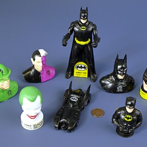 May include: A collection of eight Batman themed plastic figures, including Batman, Robin, The Joker, The Riddler, Two-Face, and Penguin. The figures are all in black and green colours and have a cartoonish style.