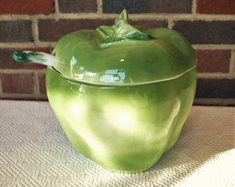 May include: Green ceramic pepper shaker with a lid and a small spoon. The pepper shaker is glazed with a light green color and has a white design.