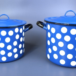 Może przedstawiać: Dwa niebieskie garnki emaliowane w białe grochy. Każdy garnek ma pasującą pokrywkę i czarne uchwyty. Garnki są w różnych rozmiarach i nadają się do gotowania. Garnki to klasyczny element wyposażenia kuchni.