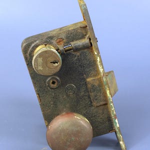 Peut inclure: Un ancien verrou de porte de la marque Reading, avec un bouton en laiton terni. Le métal est sombre et présente des signes de rouille et d'usure. La serrure, de forme rectangulaire, semble ancienne.
