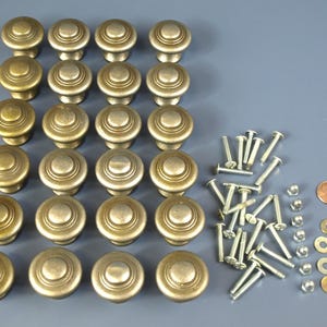 May include: A set of 20 antique brass cabinet knobs with a raised circular design. The knobs are arranged in rows and come with screws and washers.