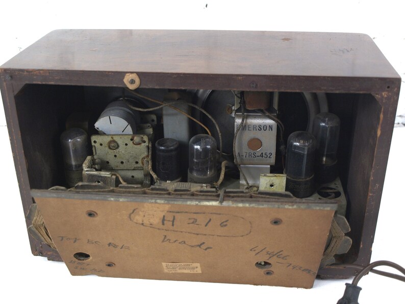 Puede incluir: Una radio Emerson vintage con un gabinete de madera. La parte posterior de la radio est&aacute; abierta, revelando los componentes internos, incluidos varios tubos de vac&iacute;o y un altavoz. La radio tiene una etiqueta que dice "Emerson 47RS-452" y "H216" escrito en la parte posterior.
