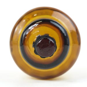 Puede incluir: Una vista superior de un objeto redondo de vidrio &aacute;mbar que presenta un centro circular de color marr&oacute;n oscuro rodeado por un anillo de color marr&oacute;n dorado transl&uacute;cido. El vidrio tiene una superficie lisa y reflectante con un borde festoneado.