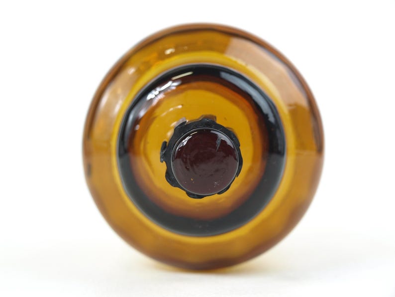Puede incluir: Una vista superior de un objeto redondo de vidrio &aacute;mbar que presenta un centro circular de color marr&oacute;n oscuro rodeado por un anillo de color marr&oacute;n dorado transl&uacute;cido. El vidrio tiene una superficie lisa y reflectante con un borde festoneado.