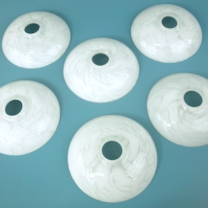 May include: A set of six circular glass lamp shades featuring a white and translucent marbled pattern. Each shade has a smooth, domed shape with a centered circular opening at the top, designed for light fixture installation and light diffusion.