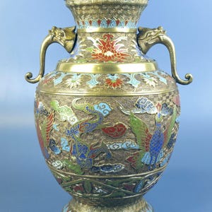 May include: An antique bronze vase with detailed enamel work. The vase has dragon-shaped handles and is decorated with colourful dragons, phoenixes, and floral designs. The vase has a wide base and a flared rim, demonstrating traditional artistry.