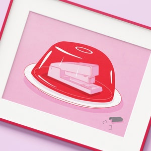 以下が含まれることがあります： 白いステープラーが入った赤いゼラチン型。型は白い皿の上にあり、背景は白です。