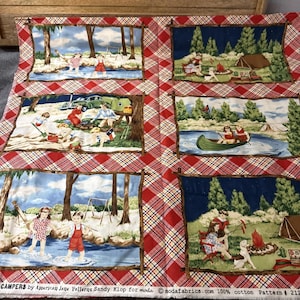 May include: A fabric panel with six illustrated camping scenes, each framed in brown against a red and white plaid backdrop. The scenes show people by a river, a campfire, and a tent. The text "CAMPERS" is visible. The fabric is 100% cotton.