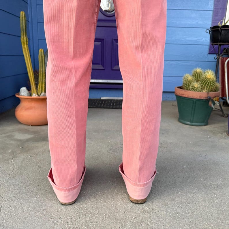 K&ouml;nnte beinhalten: Nahaufnahme einer rosa Cordhose mit umgeschlagenen S&auml;umen. Die Hose hat ein klassisches, ma&szlig;geschneidertes Design und ein weiches, strukturiertes Aussehen. Die Farbe ist ein ged&auml;mpftes, staubiges Rosa, geeignet f&uuml;r Freizeit- oder halbformelle Anl&auml;sse.