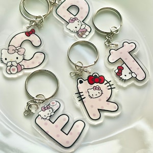 May include: Clear acrylic keychains featuring letters C, E, P, R, and T, each adorned with a pink polka-dot design and a Hello Kitty character. The keychains have silver metal rings.