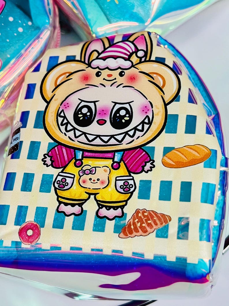 K&ouml;nnte beinhalten: Ein klarer, schillernder Rucksack mit einem Cartoon-B&auml;r-Design. Der B&auml;r tr&auml;gt einen gelben Overall mit einem B&auml;rengesicht. Der Rucksack hat einen blau-wei&szlig; gestreiften Hintergrund mit Bildern von Donut, Croissant und Brot.