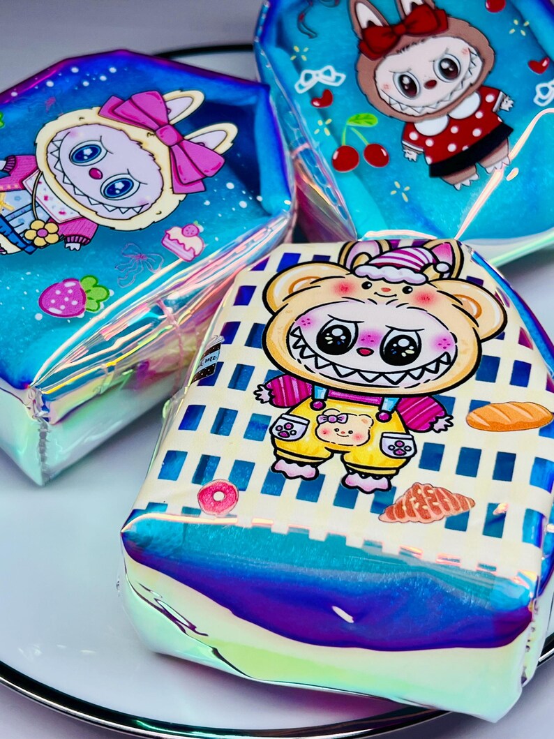 K&ouml;nnte beinhalten: Drei schillernde Kosmetiktaschen mit Cartoon-Charakter-Designs. Eine Tasche zeigt einen B&auml;ren in Latzhosen, eine andere ein H&auml;schen mit einer Schleife und die dritte ein H&auml;schen in einem roten gepunkteten Kleid. Die Taschen haben einen holografischen Glanz.