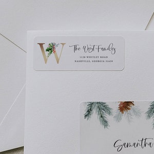 Könnte beinhalten: Weißer Umschlag mit zwei Adressetiketten. Das obere Etikett lautet "The West Family" mit einer Adresse. Das untere Etikett lautet "Samantha Roberts" mit einer Adresse. Beide Etiketten haben florale und Tannenzapfen-Elemente.