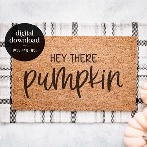 May include: A brown coir doormat with the text "Hey there pumpkin" in black lettering. The doormat is on a white and black checkered fabric with two small white pumpkins.