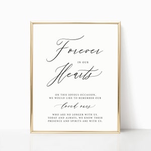 May include: A framed sign with the words "Forever in our Hearts" in elegant script. The sign includes additional text below, with a gold-colored frame. The background is a soft cream color.