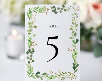 Pode incluir: Cartão branco com uma borda de folhas verdes e o texto "TABLE 5" em fonte preta. O cartão é exibido em um pequeno cavalete de madeira.