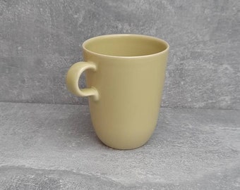 May include: A pale yellow ceramic mug with a rounded body and a curved handle. The mug has a smooth, matte finish and a simple, minimalist design. The mug is suitable for coffee, tea, or other beverages.