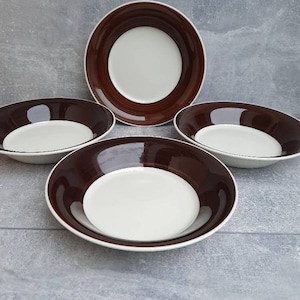 May include: Four ceramic bowls with a white interior and a dark brown rim. The bowls are arranged on a gray surface. The bowls have a simple, elegant design, suitable for serving soups, salads, or other dishes.