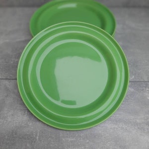 May include: Two bright green ceramic plates. The plates are round with a slightly raised rim and concentric rings. The plates are a solid, glossy green color. The plates are on a gray surface.