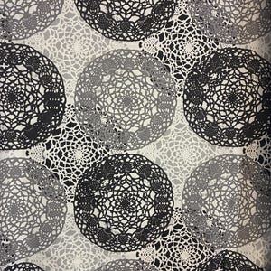 Może przedstawiać: Tkanina z powtarzającym się wzorem dużych, okrągłych wzorów przypominających serwetki w odcieniach czerni, szarości i bieli. Złożone wzory przypominające koronkę tworzą interesującą wizualnie i teksturowaną powierzchnię. Tło jest jaśniejszym odcieniem bieli.