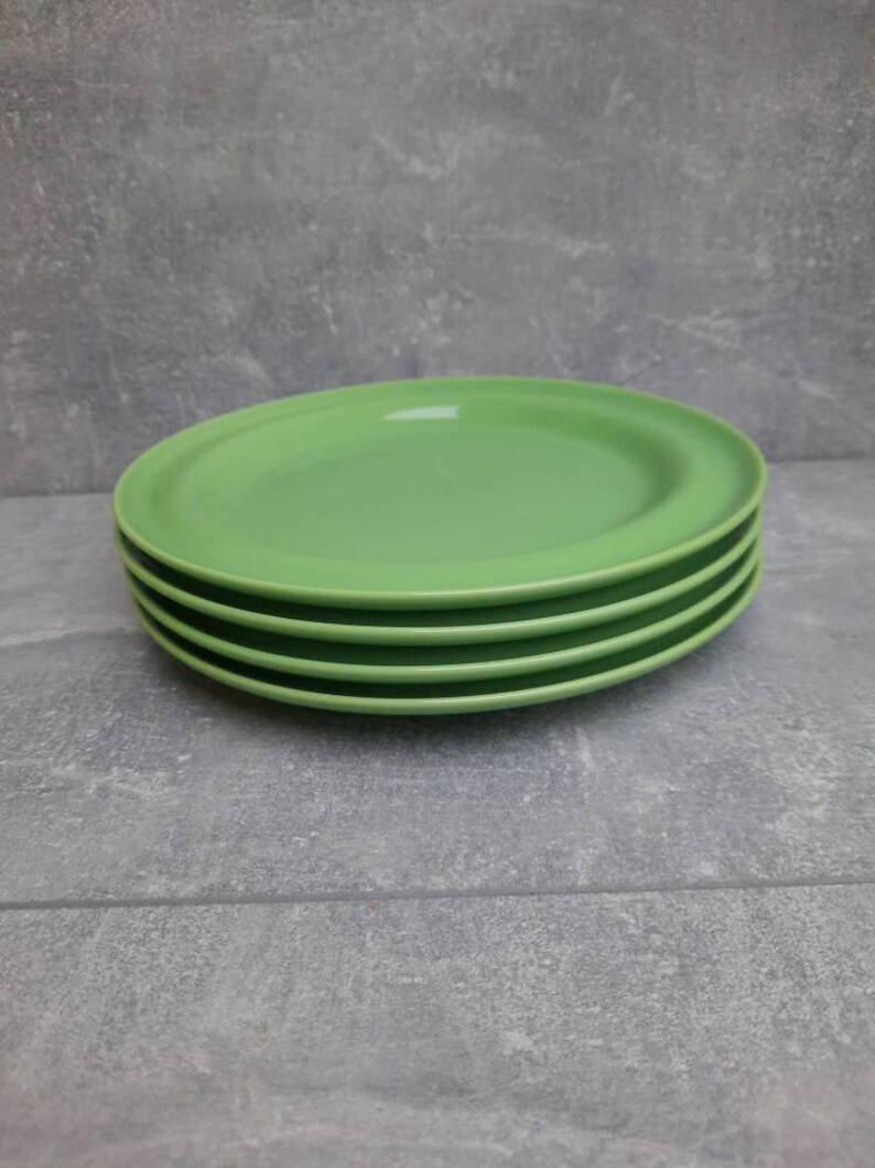 May include: A stack of four oval-shaped, light green plates. The plates are stacked neatly on top of each other, with a slight lip around the edge. The plates are a solid, bright green color.