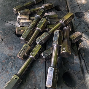 May include: A collection of metallic, hexagonal-shaped tools with a dark, weathered finish. Each tool features engraved text reading YES and NO on opposing sides, along with small circular indentations and a threaded cylindrical midsection.