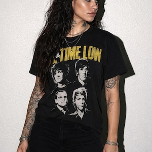 May include: A black short-sleeve t-shirt featuring the yellow text "ALL TIME LOW" printed above a black and white graphic illustration of four band members. The shirt has a crew neckline and a standard fit, showcasing a vintage-inspired band merchandise design.