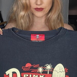 May include: Black t-shirt with a red and white graphic of a pink dragon with the text "Pink Dragon Tropical-Deco & Rock'n'Roll South Cat Street 23-23-1 Harajuku, Tokyo".