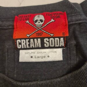 May include: A black t-shirt with a red and white label that says "Cream Soda" with a skull and crossbones graphic. The label also says "Go Fast To Live" and "Too Young To Die". The label has the year 1967 on it. The t-shirt is size large and is made of 100% pre-shrunk cotton.