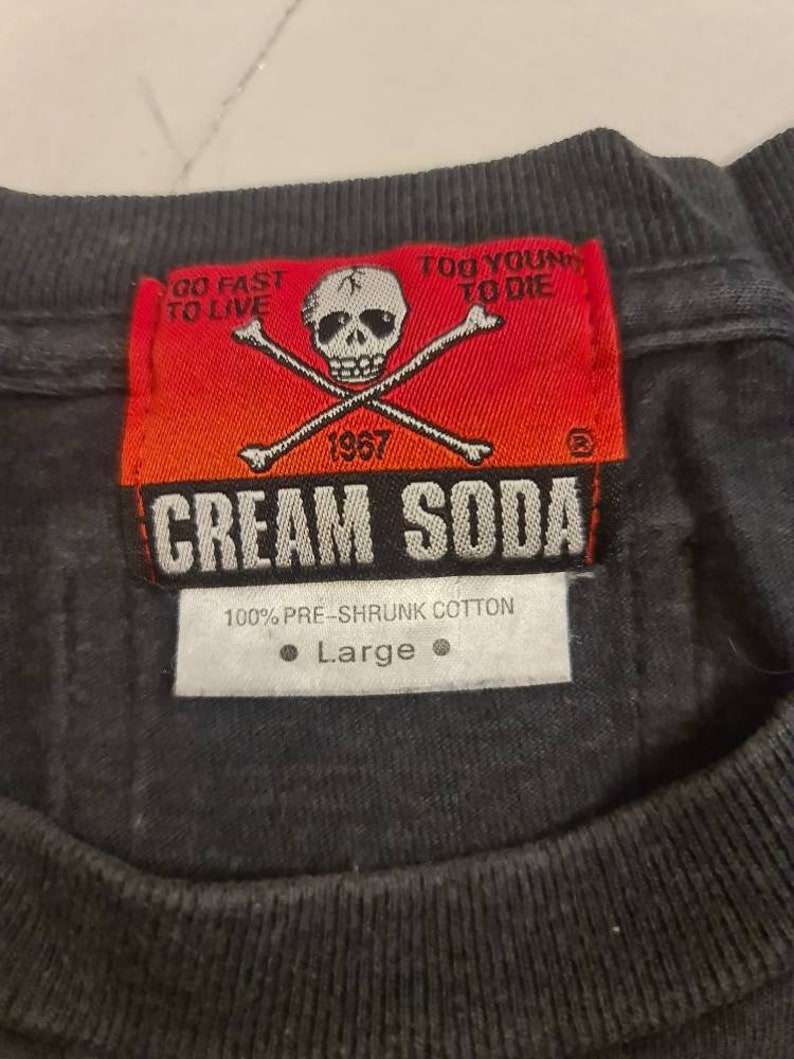 May include: A black t-shirt with a red and white label that says "Cream Soda" with a skull and crossbones graphic. The label also says "Go Fast To Live" and "Too Young To Die". The label has the year 1967 on it. The t-shirt is size large and is made of 100% pre-shrunk cotton.