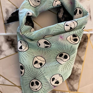 Puede incluir: Un pañuelo azul claro con un patrón repetido de caras de Jack Skellington en blanco y negro de la película Pesadilla antes de Navidad. El pañuelo tiene un borde con un patrón en blanco y negro.