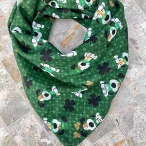 May include: Green bandana with a repeating pattern of white dogs wearing green hats and holding shamrocks. The background is a green and gold shamrock pattern.