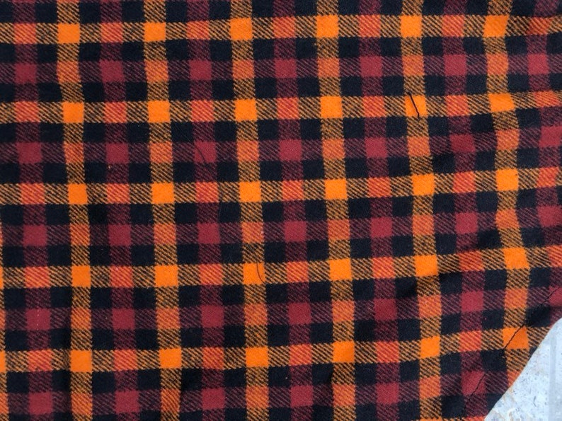 May include: Orange, black, and burgundy plaid fabric with a woven texture.