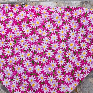 May include: Pink fabric with a white daisy pattern. The daisies have yellow centers and light purple petals. The fabric has a small white polka dot pattern.