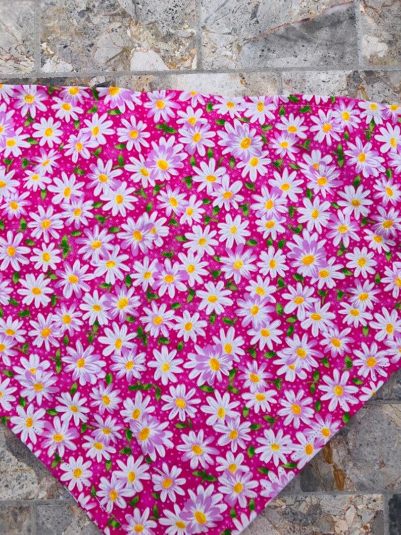 May include: Pink fabric with a white daisy pattern. The daisies have yellow centers and light purple petals. The fabric has a small white polka dot pattern.