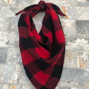 May include: Red and black plaid bandana with a knotted design. The bandana is made of a soft, woven fabric.