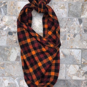 May include: A black, orange, and red plaid bandana tied in a knot. The bandana is made of a soft, fuzzy fabric.