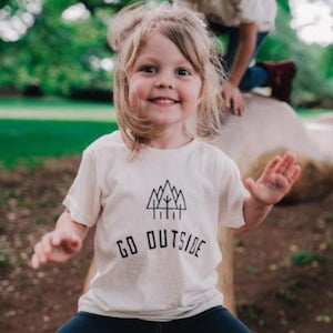 May include: A white t-shirt with a black graphic of a mountain range and trees. The text "GO OUTSIDE" is printed below the graphic.